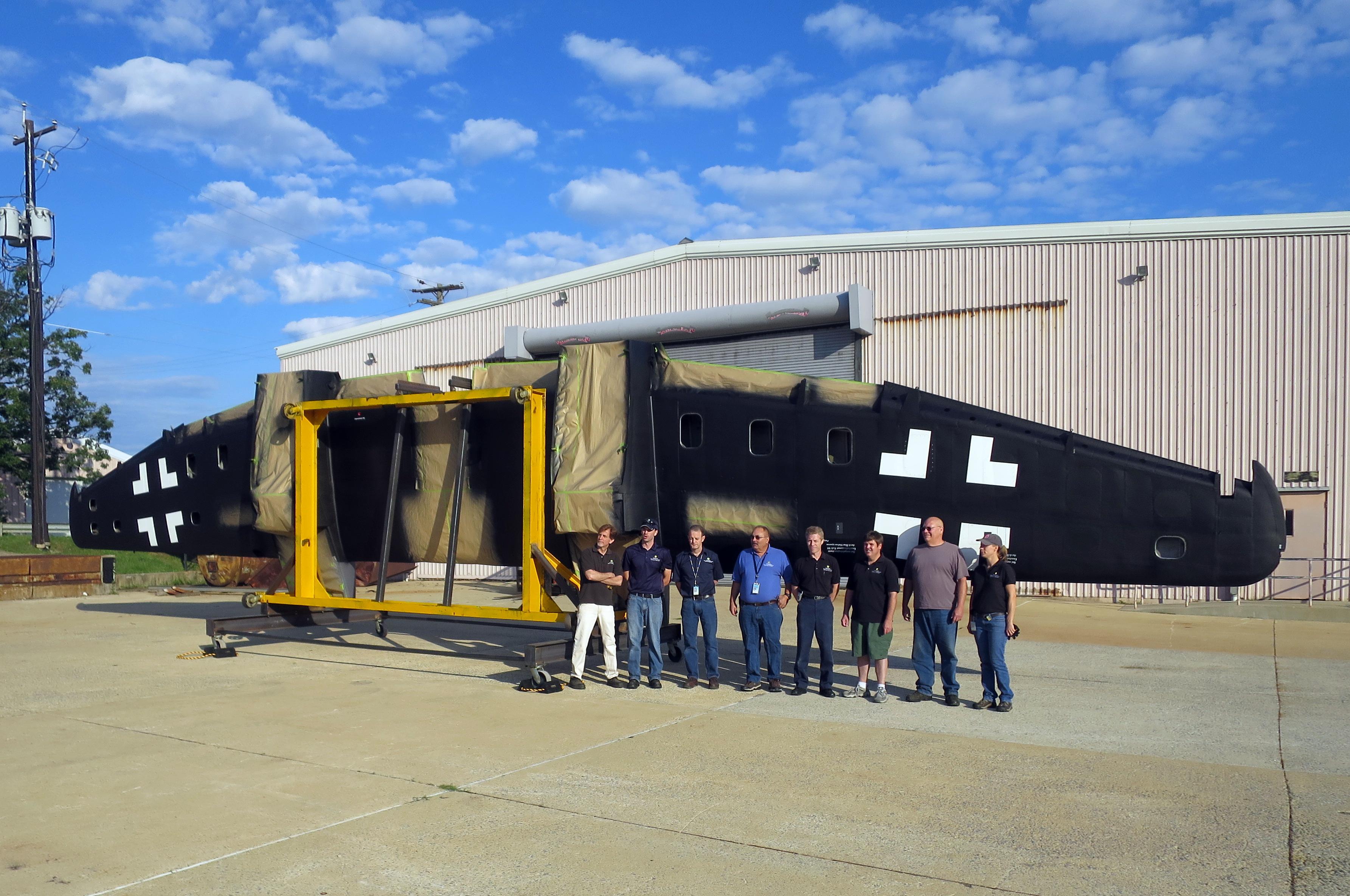 NASM's Heinkel He-219 Restoration Update 11 The wing rotation crew. Seventy years after their original production, the He 219's wing looks like new. Note the position of the Balkenkreuz on the outer wing panels. Although Luftwaffe regulations routinely specified that this insignia be placed parallel to the leading edge of the wing, Heinkel located it in a slightly different position, parallel to the spar, which was exactly reproduced by NASM experts. Clearly visible are the blue horizontal and yellow vertical stand the wing is mounted to. (photo via NASM)