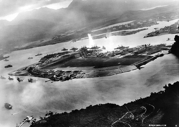Commemorating the 72nd Anniversary of the Attack on Pearl Harbor 10 7 December 1941-Photograph taken from a Japanese plane during the torpedo attack on ships moored on both sides of Ford Island shortly after the beginning of the Pearl Harbor attack. View looks about east, with the supply depot, submarine base and fuel tank farm in the right center distance. A torpedo has just hit USS West Virginia on the far side of Ford Island (center). Other battleships moored nearby are (from left): Nevada, Arizona, Tennessee (inboard of West Virginia), Oklahoma (torpedoed and listing) alongside Maryland, and California. On the near side of Ford Island, to the left, are light cruisers Detroit and Raleigh, target and training ship Utah and seaplane tender Tangier. Raleigh and Utah have been torpedoed, and Utah is listing sharply to port. Japanese planes are visible in the right center (over Ford Island) and over the Navy Yard at right. U.S. Navy planes on the seaplane ramp are on fire. Japanese writing in the lower right states that the photograph was reproduced by authorization of the Navy Ministry. (Official U.S. Navy photograph)