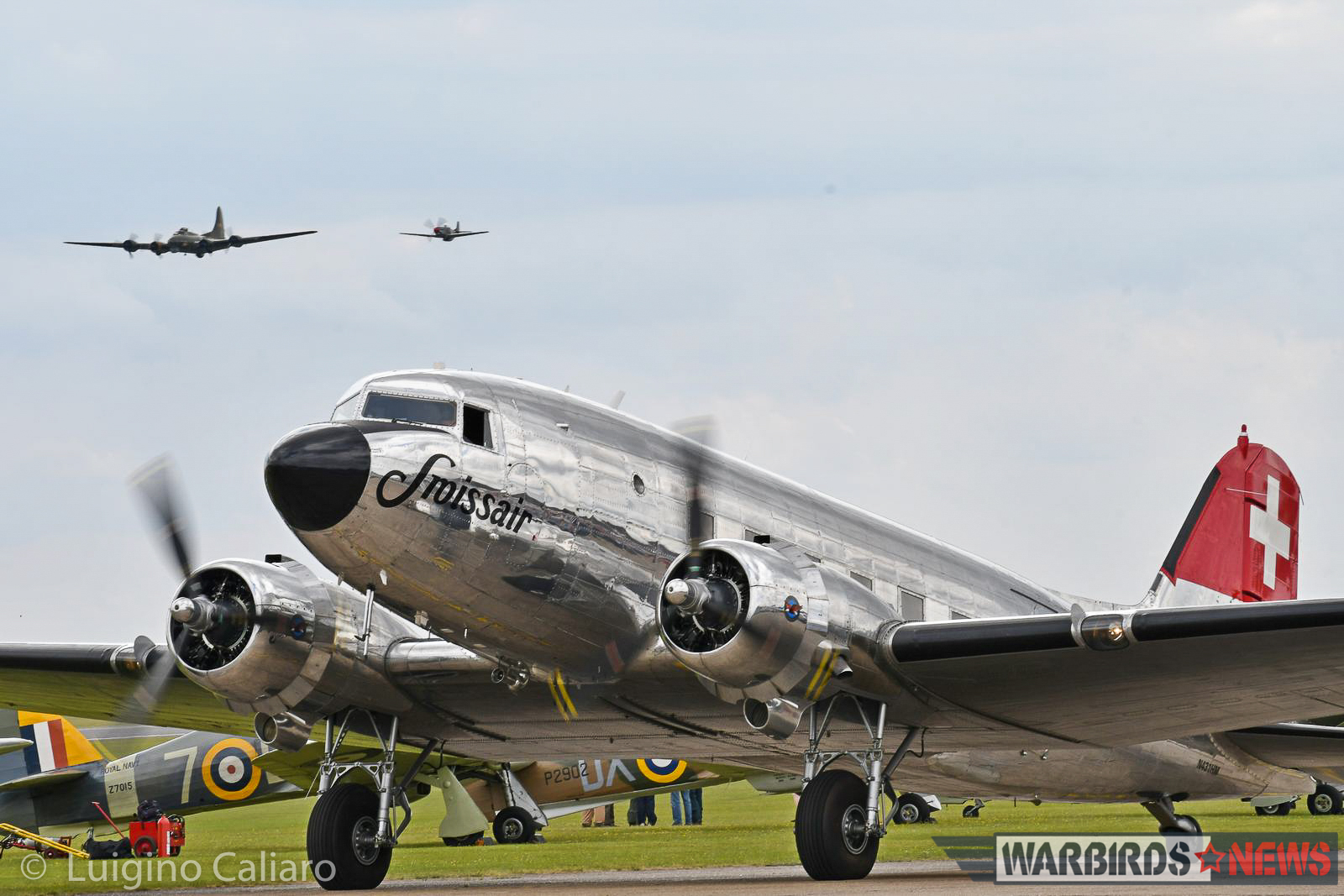 Flying Legends 2017 - Air Show Report 16 A fabulously maintained Swiss-based DC-3 taxies past a row of Hawker Hurricanes while B-17G 'Sally-B' flies overhead in company of a 'Little Friend'. (photo by Luigino Caliaro)
