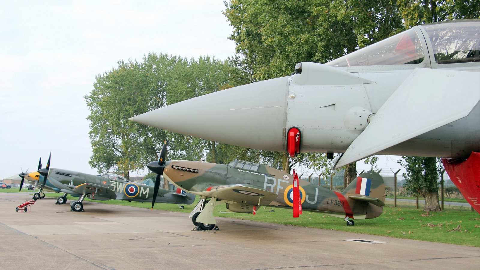 The Battle of Britain Memorial Flight Hosts 2025 Members’ Day at RAF Coningsby 12 Static line up of BBMF fighters under the nose of a Typhoon FGR4. Photo Clive Rowley