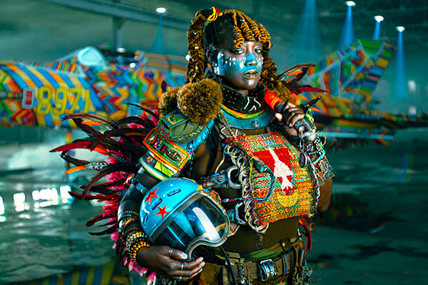 From Warplane to Work of Art: The Stunning MiG-21 Project Premieres June 21 12 The MiG 21 Project Ruacana Raider Returns staged photo of woman wearing custom regalia in front of the beaded MiG 21 fighter. Photo courtesy The MiG 21 Project