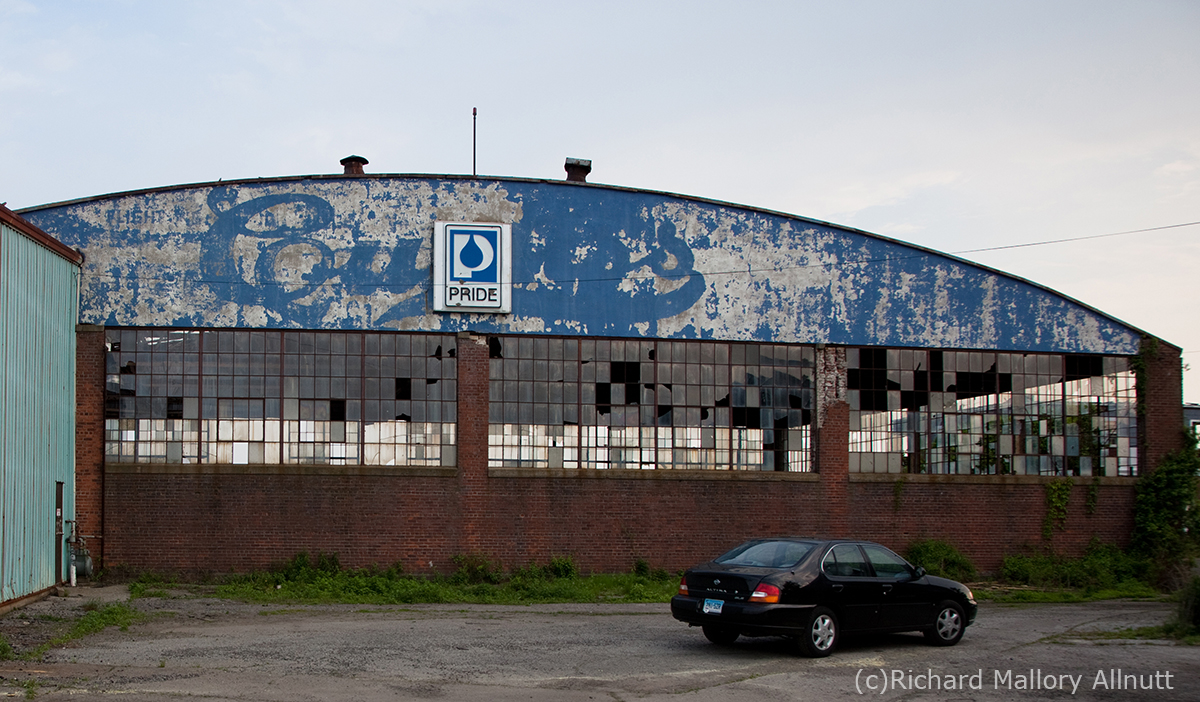 Curtiss Hangar Restoration Groundbreaking Ceremony 14 The north side of The Curtiss Hangar as it appeared in May, 2010. The paint has peeled significantly to reveal the old Curtiss logo from the late 1920's when the Curtiss Flying School this operated from this hangar. The greenish structure to the left is a lean-to added to the hangar some time after the Curtiss days. (photo Richard Mallory Allnutt)